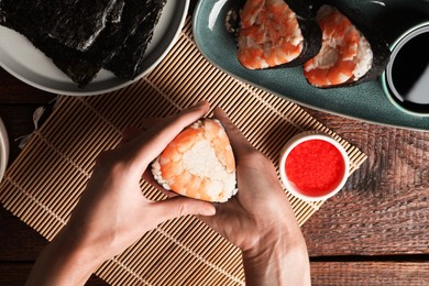 Photo of Woman holding tasty onigiri (Japanese rice ball) with shrimp at wooden table, top view