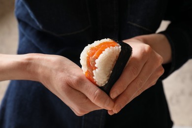 Photo of Woman with tasty onigiri (Japanese rice ball) indoors, closeup