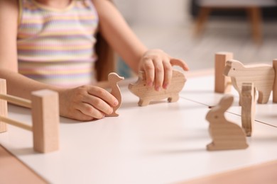 Photo of Motor skills development. Little girl playing with wooden animals at table indoors, closeup