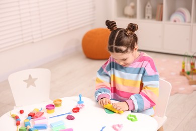 Photo of Motor skills development. Little girl playing with colorful dough at table indoors