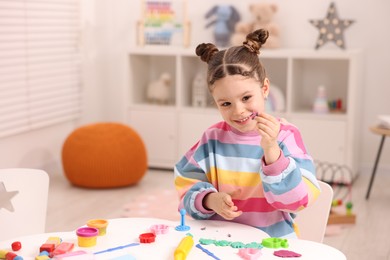 Photo of Motor skills development. Little girl playing with colorful dough at table indoors