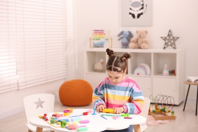 Photo of Motor skills development. Little girl playing with colorful dough at table indoors