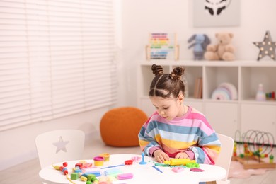 Photo of Motor skills development. Little girl playing with colorful dough at table indoors