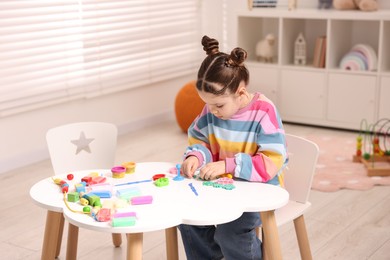 Photo of Motor skills development. Little girl playing with colorful dough at table indoors