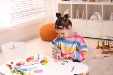 Photo of Motor skills development. Little girl playing with colorful dough at table indoors