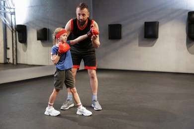 Photo of Girl in protective gloves having boxing practice with her coach at training center. Space for text