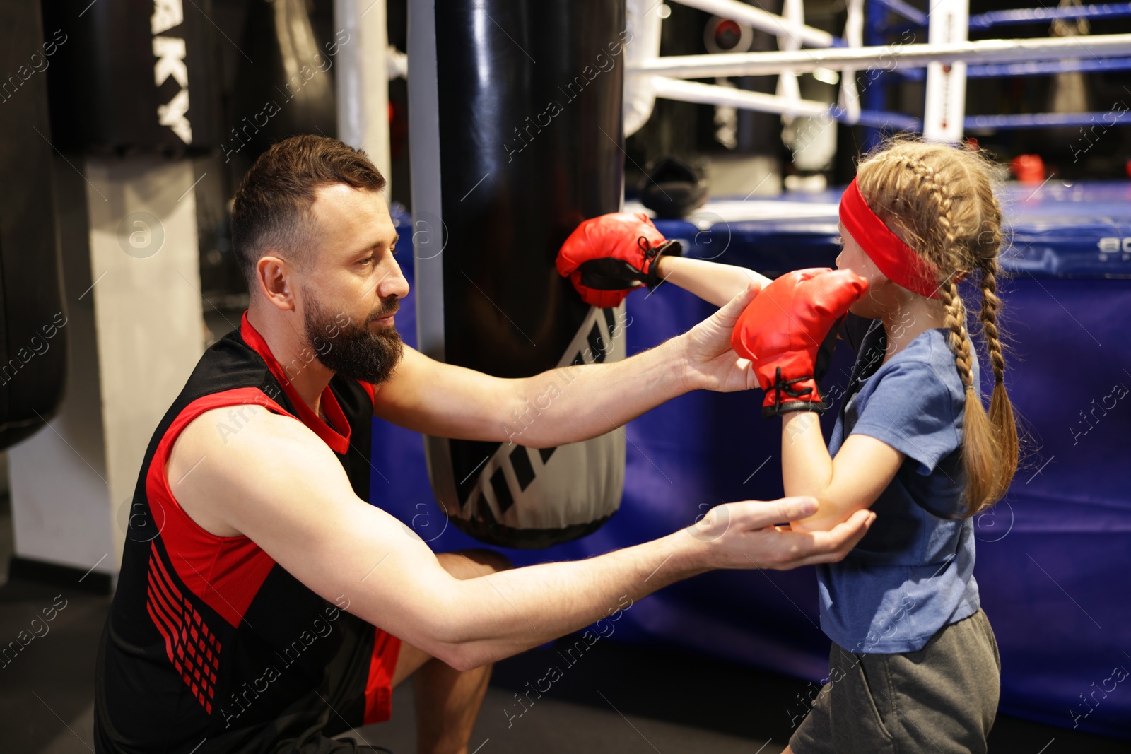 Photo of Girl in protective gloves having boxing practice with her coach at training center