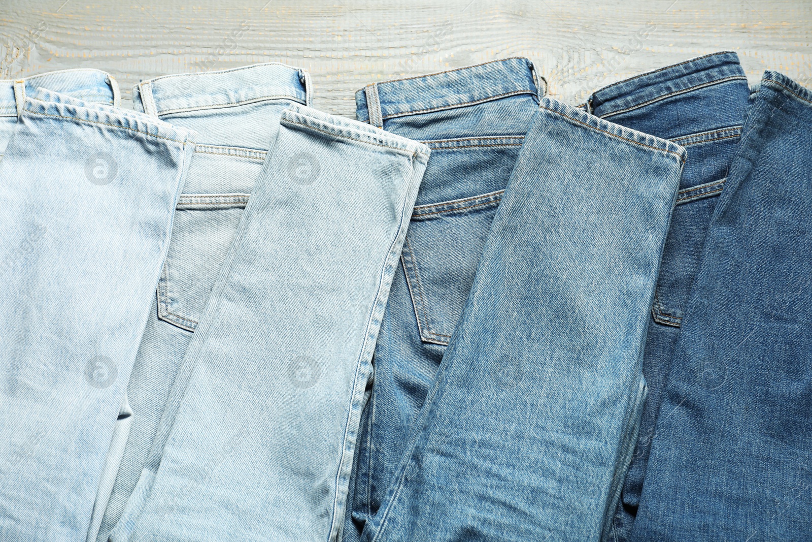 Different stylish jeans on grey wooden background, flat lay Photo of Different stylish jeans on grey wooden background, flat lay