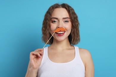 Photo of Smiling woman with fake paper mustache on light blue background