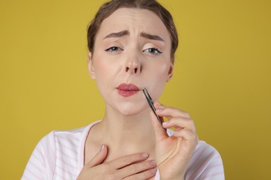 Photo of Beautiful woman plucking her mustache with tweezers on light green background