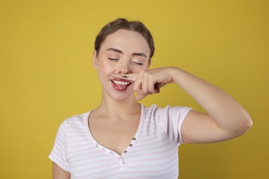 Photo of Funny woman holding finger with drawn mustache above lips on light green background