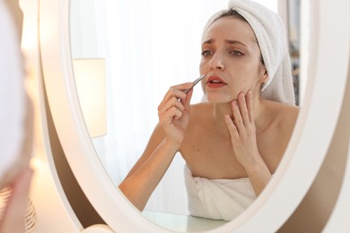 Photo of Beautiful woman plucking her mustache with tweezers near mirror at home