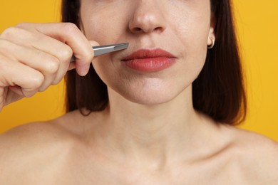 Photo of Woman plucking her mustache with tweezers on orange background, closeup