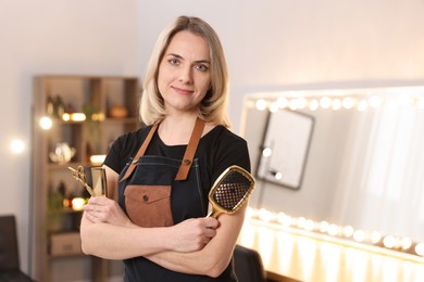 Photo of Hairdresser with brush, comb and scissors in beauty salon