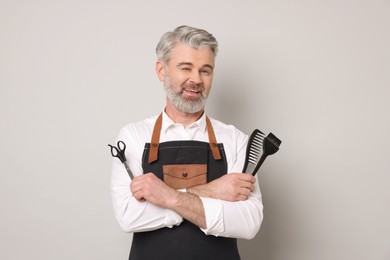 Photo of Smiling hairdresser with scissors, comb and hair dye brush on gray background