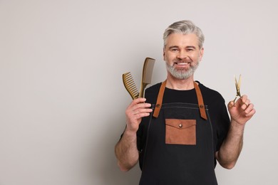 Photo of Smiling hairdresser with scissors and combs on gray background, space for text