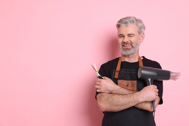 Photo of Smiling hairdresser with dryer and scissors on pink background, space for text