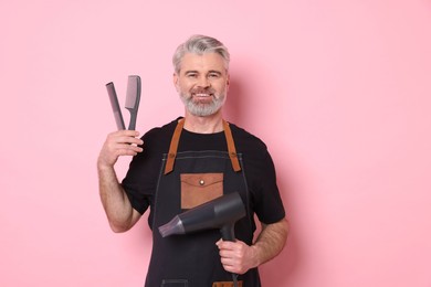 Photo of Smiling hairdresser with dryer and combs on pink background