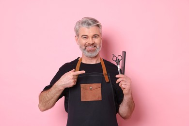 Photo of Smiling hairdresser with scissors and comb on pink background