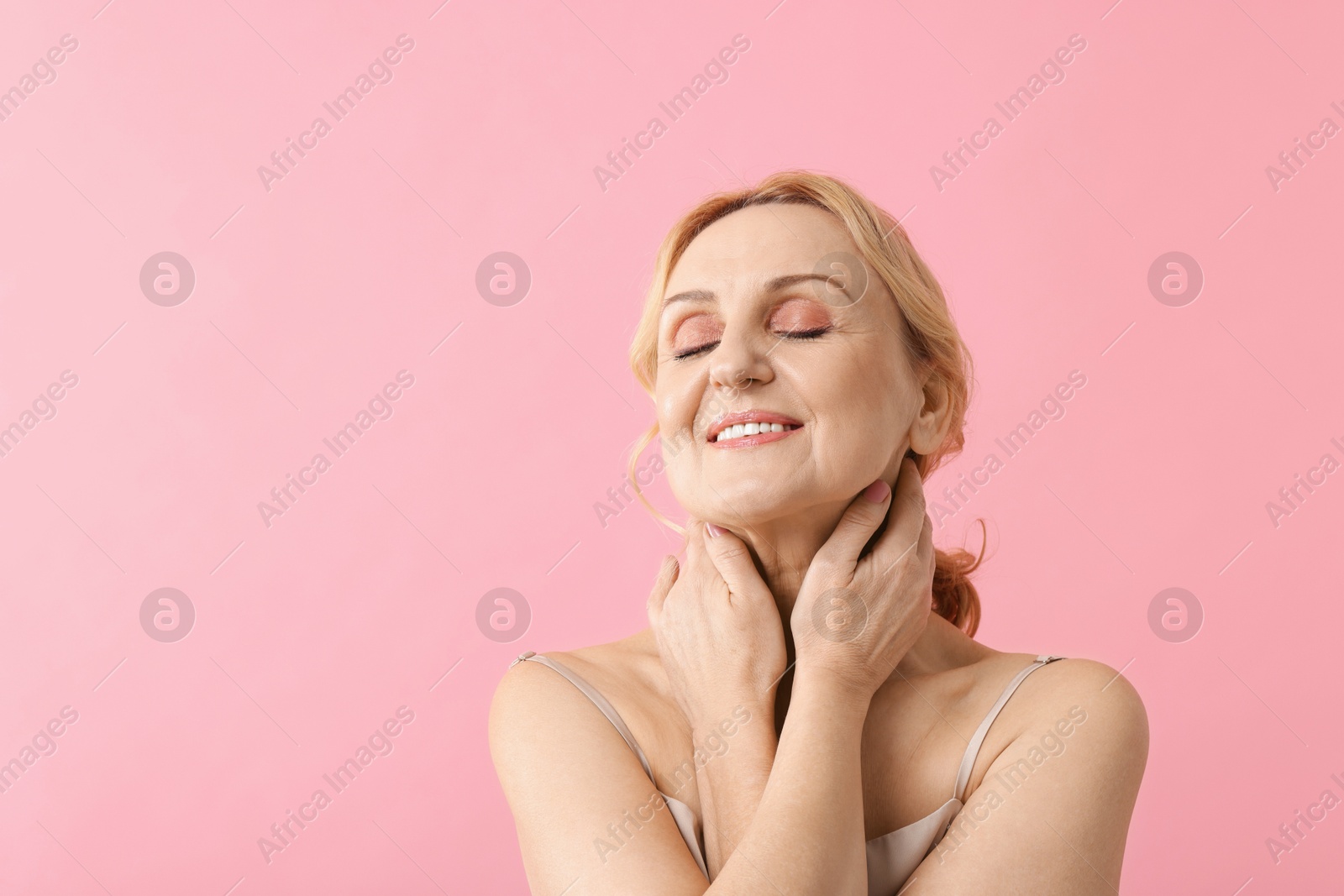 Photo of Smiling middle aged woman on pink background. Space for text