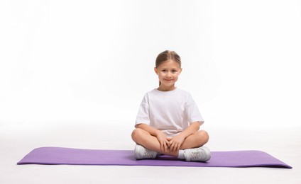 Photo of Cute little girl sitting on fitness mat against white background