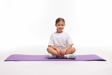 Photo of Cute little girl sitting on fitness mat against white background