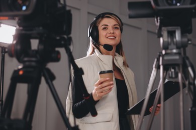 Photo of Happy young camerawoman with coffee working in modern film studio