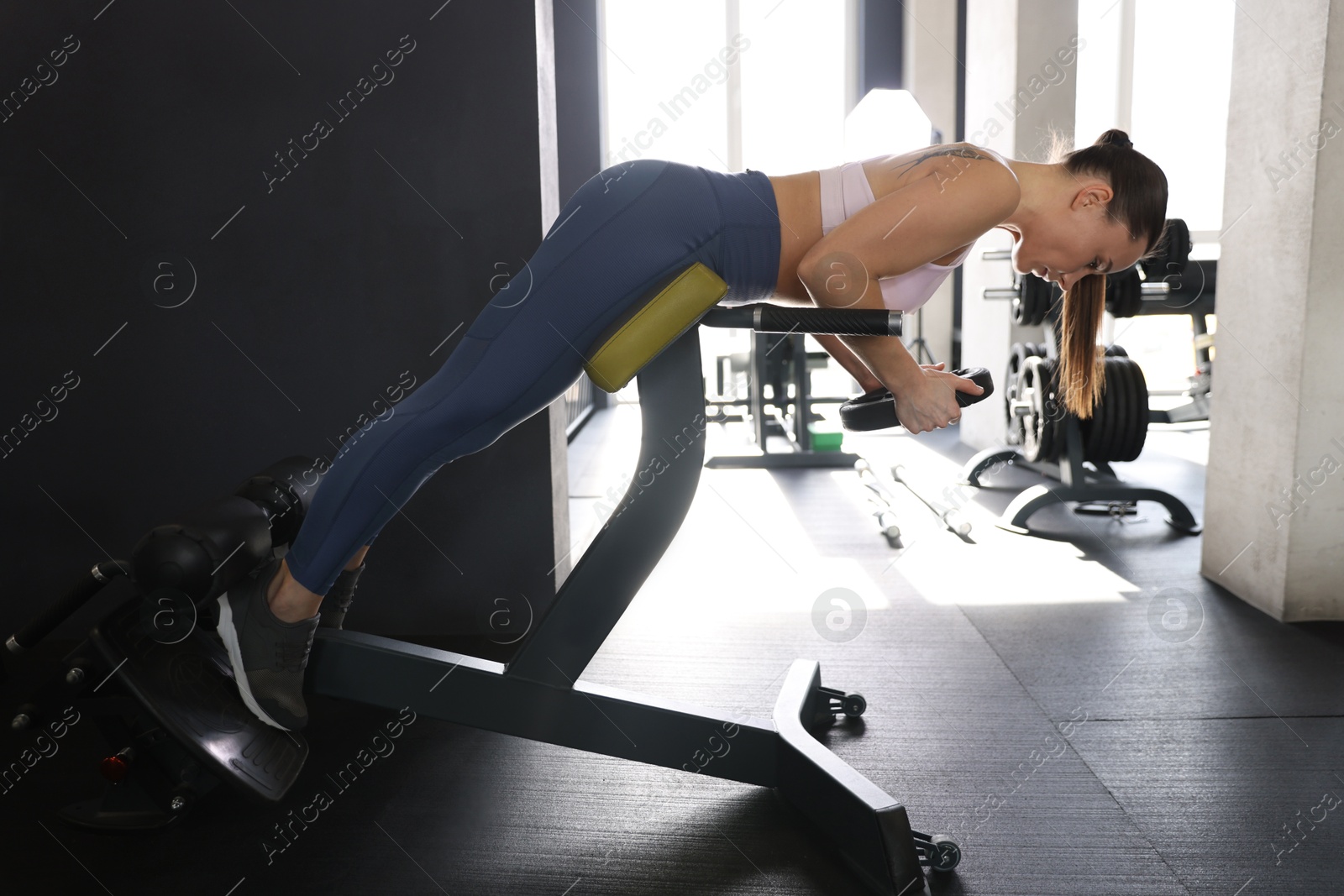 Photo of Athletic woman training with weight plate on t-bar row machine in gym