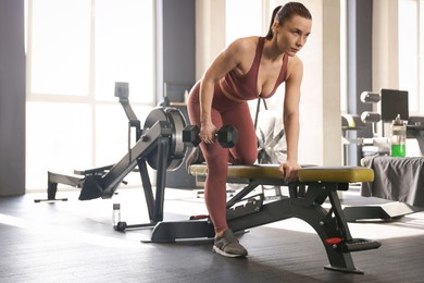 Photo of Athletic woman training with dumbbell on exercise bench in gym