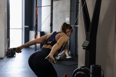 Photo of Athletic woman training with ski machine in gym, back view