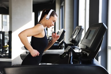 Photo of Athletic woman in headphones training on treadmill in gym