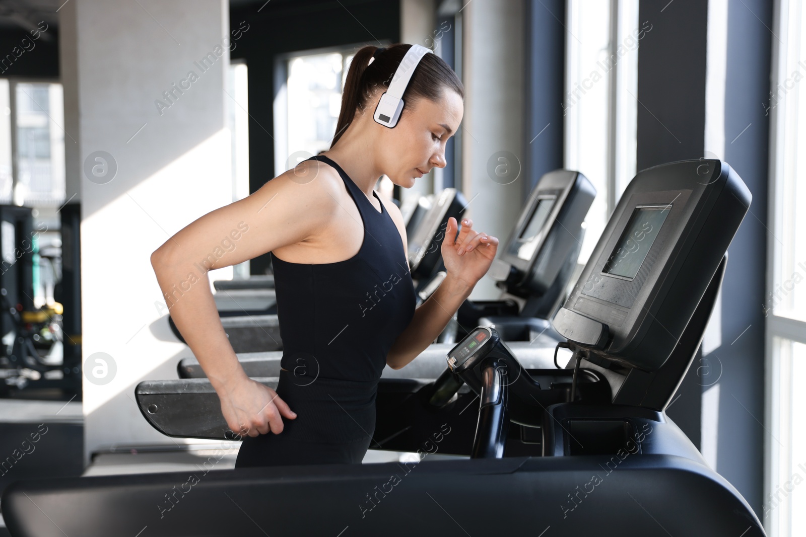 Photo of Athletic woman in headphones training on treadmill in gym