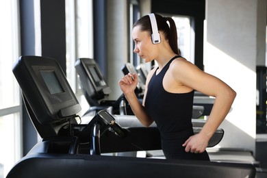 Photo of Athletic woman in headphones training on treadmill in gym