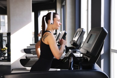 Photo of Athletic woman in headphones training on treadmill in gym