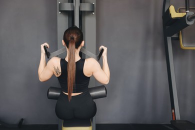 Photo of Athletic woman training on pulley machine in gym, back view