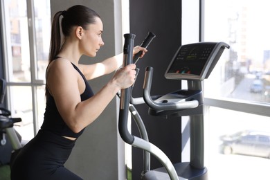 Photo of Athletic woman training on elliptical machine in gym