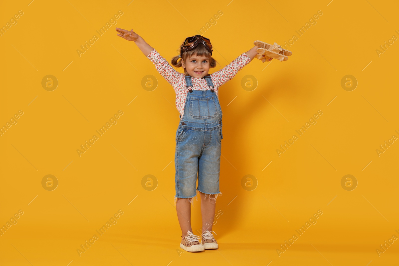 Photo of Happy little girl with toy plane on orange background