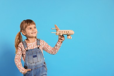 Photo of Happy little girl playing with toy plane on light blue background. Space for text