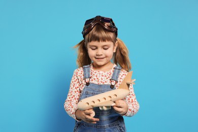 Photo of Cute little girl with toy plane on light blue background