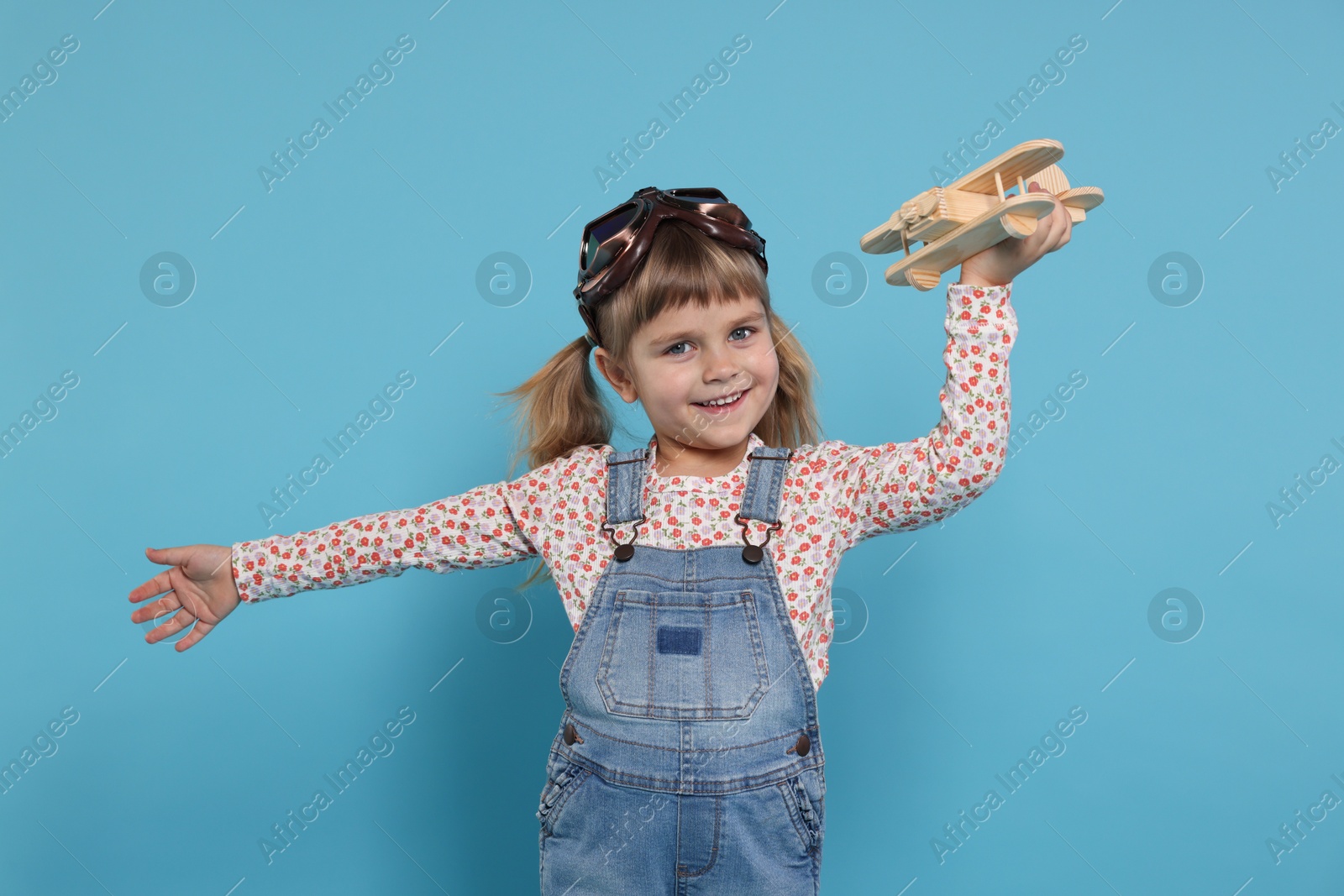 Photo of Happy little girl playing with toy plane on light blue background