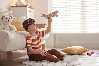 Photo of Happy little boy playing with toy plane at home