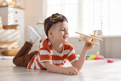 Photo of Happy little boy playing with toy plane at home