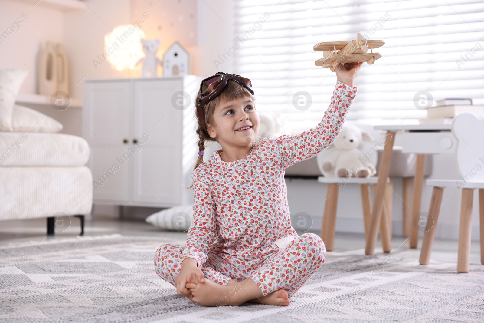 Photo of Cute little girl playing with toy plane at home