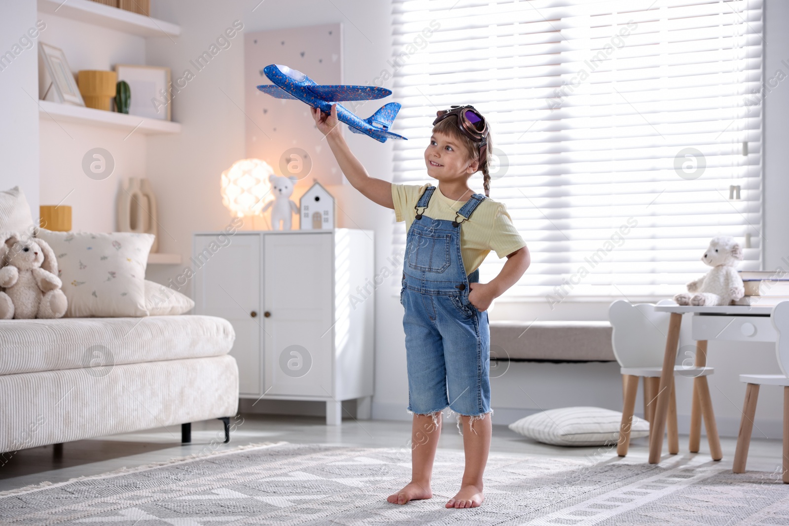 Photo of Cute little girl playing with toy plane at home