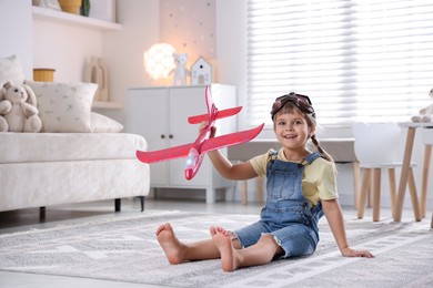 Photo of Cute little girl playing with toy plane at home