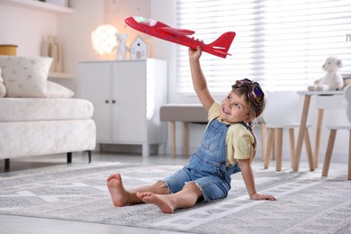 Photo of Cute little girl playing with toy plane at home