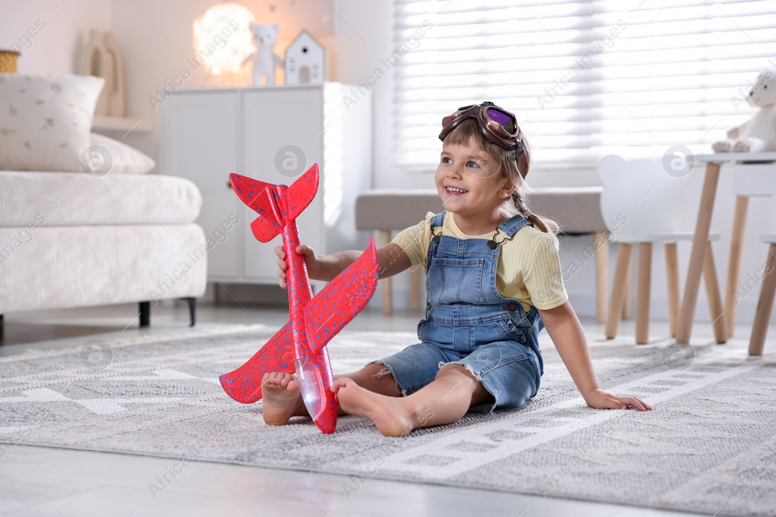 Photo of Cute little girl playing with toy plane at home