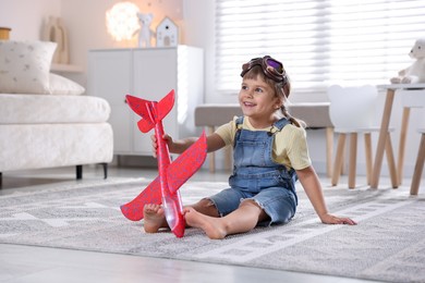 Photo of Cute little girl playing with toy plane at home