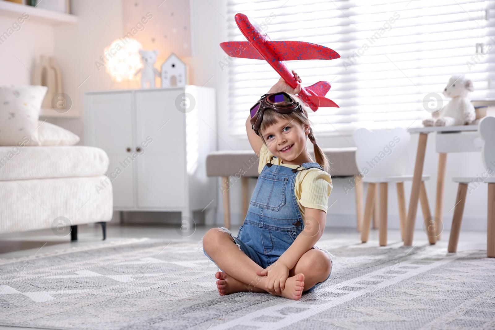 Photo of Cute little girl playing with toy plane at home