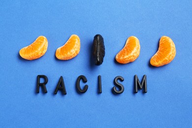 Photo of Word Racism and tangerine segments of different colors on blue background, flat lay